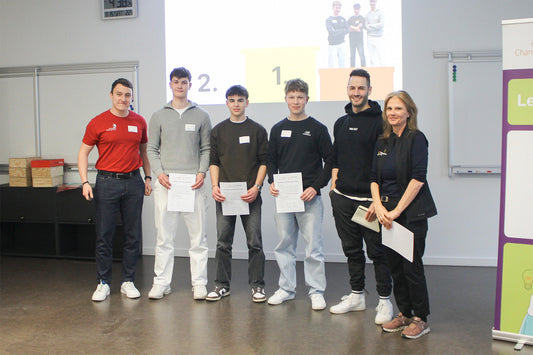 Group photo of SwissSkills participants receiving certificates during an award ceremony, with a presentation screen and banner in the background.