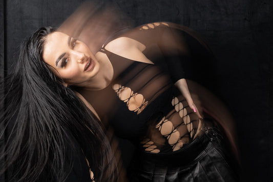 Portrait of Ely Vogt in a black cut-out top and leather skirt, captured with motion blur for a dynamic artistic effect in front of a dark backdrop