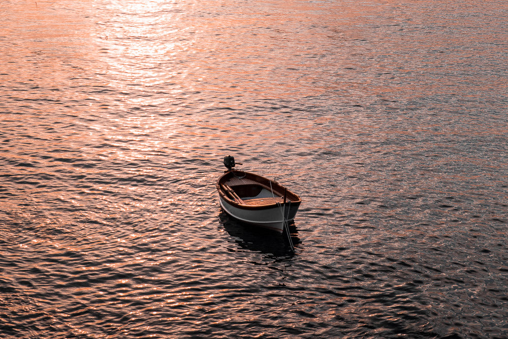 Serene wooden boat floating on calm water, reflecting the warm golden hues of the sunset, creating a peaceful and tranquil atmosphere.