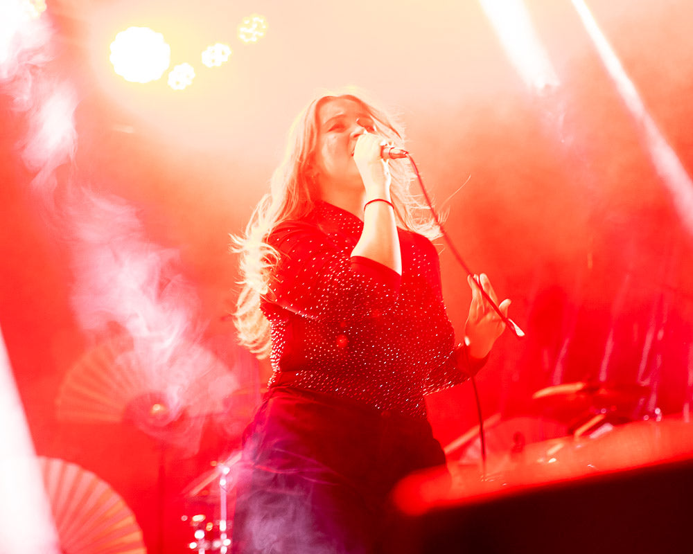 Female singer Joya Marleen performing live on stage, illuminated by intense red lighting and dramatic smoke effects, conveying energy and passion in a dynamic concert setting.