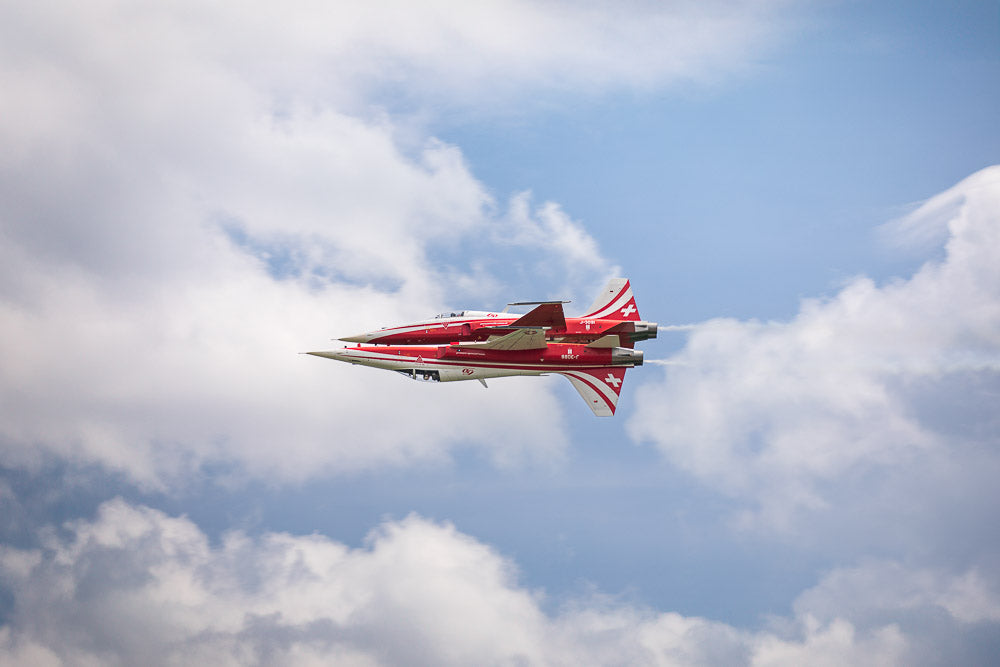 Two Swiss Air Force Patrouille Suisse fighter jets perform a precise mirror flight maneuver against a backdrop of blue sky and clouds. Aerobatic display, Swiss aviation excellence, and precision flying.