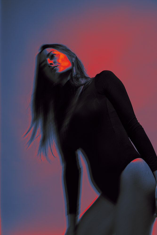 Artistic portrait of a woman in a black bodysuit, illuminated by bold red and blue lighting effects. The creative use of color contrast and motion blur adds a surreal, futuristic touch to the striking composition.