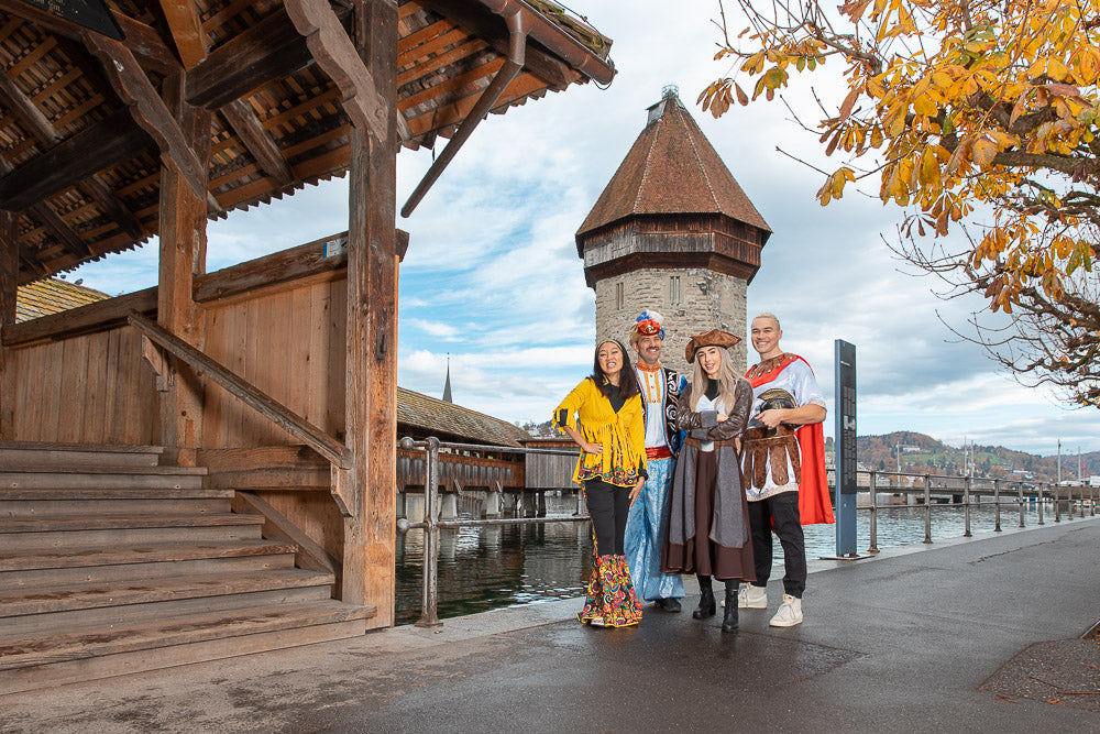 Group of people dressed in colorful historical and fantasy costumes posing near the iconic Chapel Bridge in Lucerne, Switzerland, capturing a vibrant cultural and festive atmosphere.