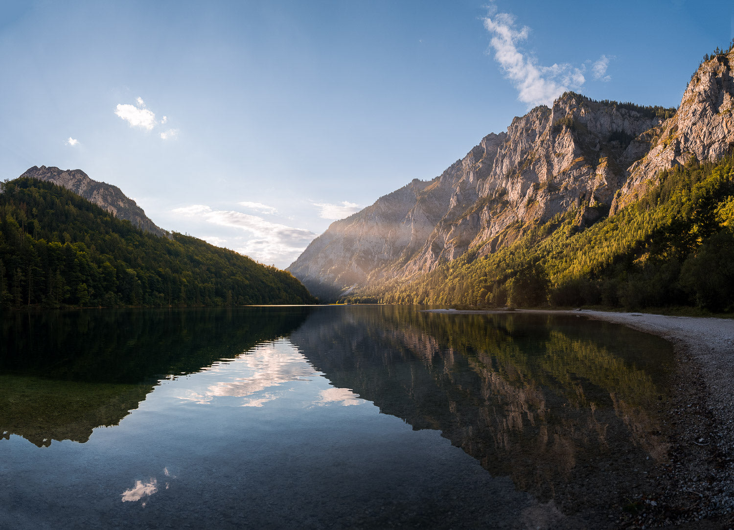 Scenic mountain lake reflecting rugged peaks and lush forests in golden sunlight, capturing the tranquility and beauty of nature in a breathtaking landscape photograph.