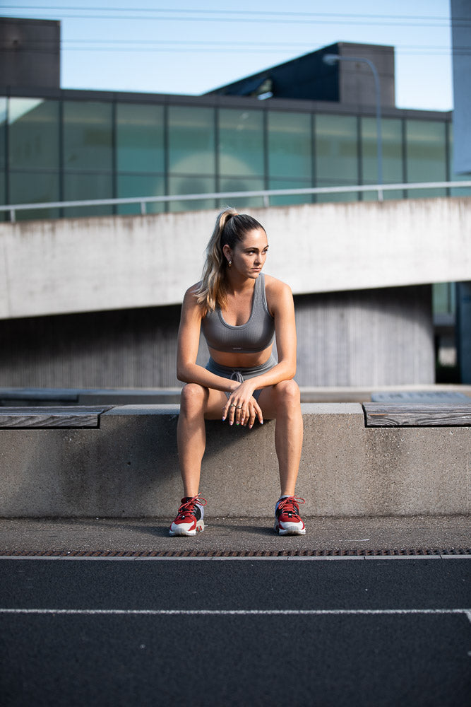 A fit young woman in sportswear sitting on a concrete ledge in an urban environment, taking a break from her workout. Capturing strength, determination, and modern fitness lifestyle.