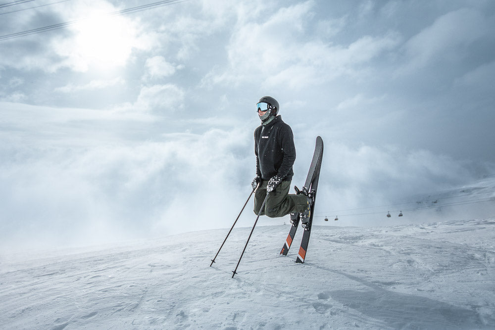 Skier with a WE•TRST Hoodie performing  on a snowy mountain with dramatic clouds in the background. Winter sports, freestyle skiing, alpine adventure, and extreme sports photography.