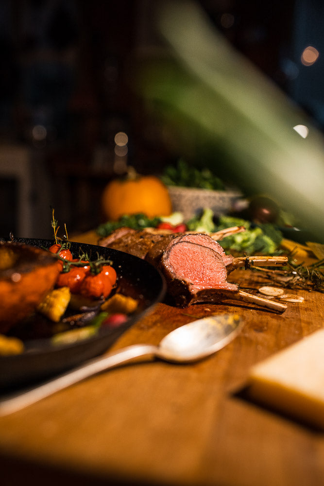 Perfectly cooked lamb rack with a pink center, plated with roasted cherry tomatoes and seasonal vegetables on a wooden cutting board, highlighting gourmet cuisine and fine dining presentation.