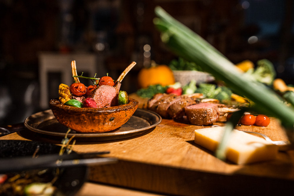 Gourmet dish featuring a lamb rack with roasted cherry tomatoes, Brussels sprouts, and corn, elegantly plated in an edible bowl on a wooden cutting board, highlighting fine dining and culinary craftsmanship.