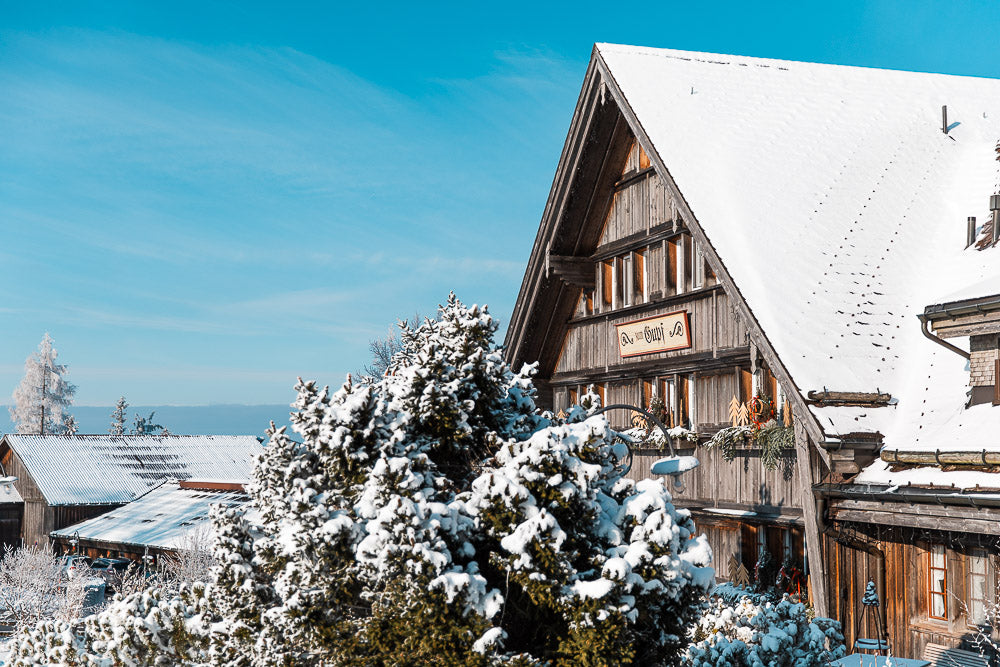 Traditional wooden alpine guesthouse Gasthaus Gupf covered in fresh snow, surrounded by winter landscape and blue skies, capturing the charm of Swiss mountain hospitality.