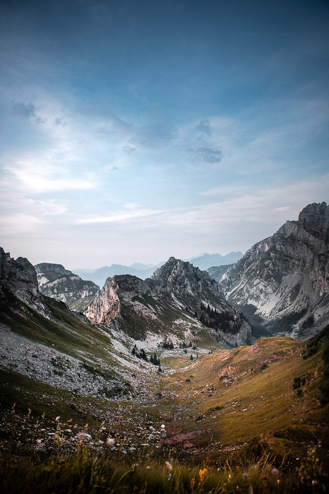 Scenic mountain landscape of Fronalpstock, Switzerland, featuring rugged peaks, lush green valleys, and a vast sky with soft cloud formations at sunrise or sunset.