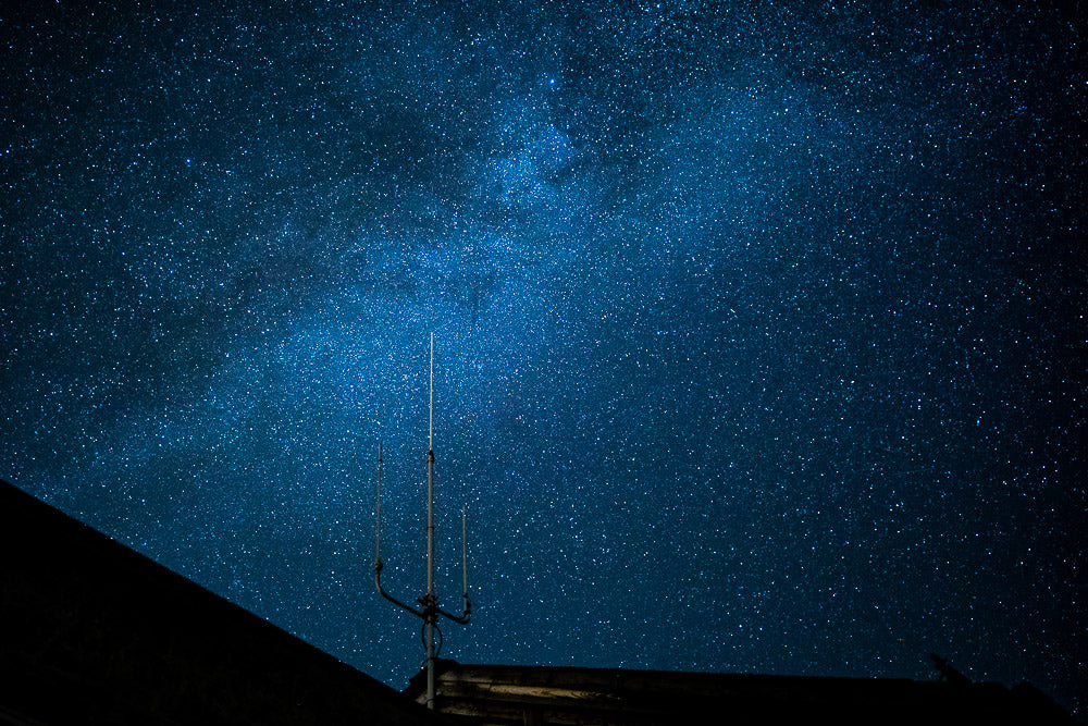 Stunning night sky filled with countless stars over a silhouetted rooftop and antenna, capturing the vastness of the Milky Way in a remote location.