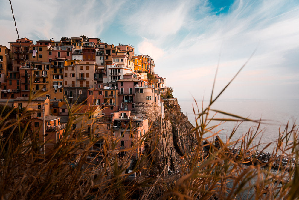 Scenic view of Manarola, one of Cinque Terre’s picturesque villages in Italy, with colorful houses perched on a rocky cliff overlooking the Ligurian Sea during sunset.